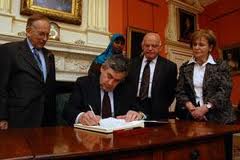 On the 2009 Holocaust Memorial Day ceremonies in Britain, Prime Minister Gordon Brown signs the Holocaust Memorial Day book of commitment watched by Lord Janner, left, and survivors Ben Helfgott and Mala Tribich, right.